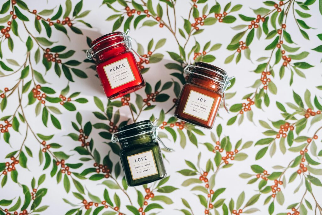 Collection of scented candles labeled Peace, Joy, Love on a leafy holiday background.